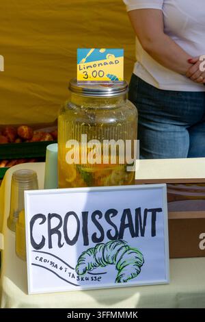 Un grand distributeur de boissons en verre rempli d'une limonade maison contenant des fruits citriques tranchés et des herbes, exposé sur une table à côté d'une note manuscrite Banque D'Images