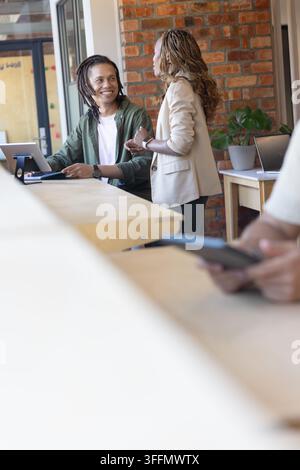 Divers collègues discutant au comptoir dans le salon, un homme utilisant une tablette, une femme en blazer beige gesticulant Banque D'Images