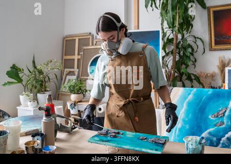Artiste féminine affinant des motifs dans une peinture en résine époxy non durcie avec un bâton de bois fin à la maison. Banque D'Images