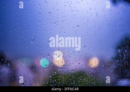 Présentation en gros plan de gouttes d'eau accrochées à une vitre pendant un orage, capturant un ciel dramatique illuminé par un éclair derrière les nuages Banque D'Images