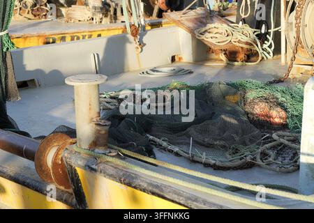 Pont de bateau de pêche montrant des filets verts et noirs emmêlés, des cordages enroulés et des bittes, mettant en évidence l'équipement essentiel pour un navire de travail Banque D'Images