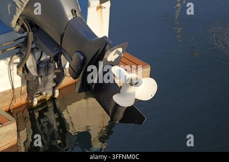 Moteur hors-bord avec hélice blanche fixée à la transom d'un bateau, partiellement immergé dans une eau bleu foncé, reflétant la lumière et offrant un transport aquatique Banque D'Images
