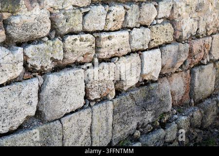 Vue rapprochée d'un vieux mur de pierre construit avec des blocs irréguliers, présentant une texture rocheuse rugueuse et usée ainsi que des motifs, convenant comme fond pour Banque D'Images