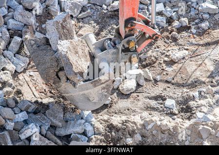 Vue rapprochée d'une pelle d'excavatrice hydraulique travaillant parmi des pierres cassées et des gravats sur un chantier de construction. L'accessoire métallique lourd est entouré Banque D'Images
