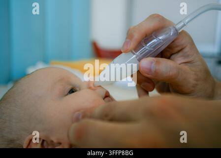 Un parent utilise soigneusement un aspirateur nasal manuel pour retirer la mucus du nez bouché d'un bébé, soutenant la santé respiratoire du nourrisson et fournissant des soins essentiels au nouveau-né en cas de congestion Banque D'Images