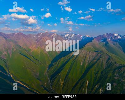 Vue aérienne capturant une chaîne de montagnes époustouflante au Kirghizistan. Des pentes dramatiques passent du terrain rocheux aux vallées verdoyantes, avec de la neige sur les sommets lointains. Banque D'Images