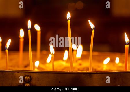Plusieurs bougies minces en cire brûlent vivement, leurs flammes dansent et créent une lumière douce et ambiante sur un fond sombre Banque D'Images