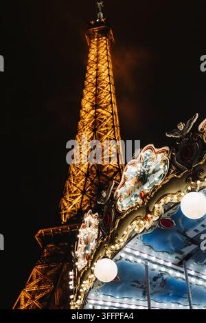 Tour Eiffel illuminée la nuit à Paris, France, s'élevant derrière un manège traditionnel orné de lumières décoratives Banque D'Images