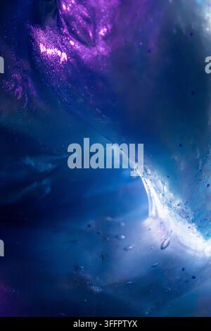 Texture liquide abstraite bleue et violette avec une vague lumineuse tourbillonnante, des gouttelettes suspendues et des nuages de pigments lumineux, créant un sous-marin cosmique Banque D'Images