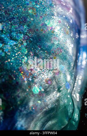 Vue macro d'une résine bleu-vert translucide remplie de paillettes hexagonales iridescentes, de particules scintillantes et de tourbillons fluides, créant un B lumineux abstrait Banque D'Images
