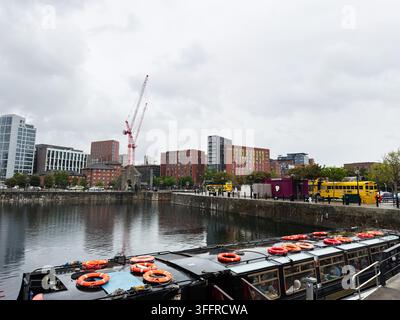 Liverpool, Royaume-Uni - 16 mai 2026 : Bateau touristique au bord de l'eau de Liverpool avec des reflets, un horizon urbain, des grues de construction et un temps nuageux. Banque D'Images