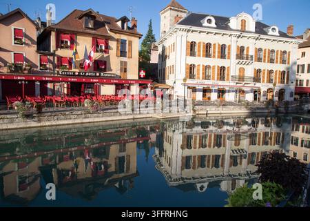 Vue diurne lumineuse des façades historiques des bâtiments se reflétant dans l'eau vitreuse du canal du Thiou dans la vieille ville d'Annecy, France. Banque D'Images