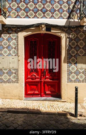 Double porte rouge vif encadrée par des carreaux décoratifs sur une façade ensoleillée de Lisbonne, Portugal. Banque D'Images