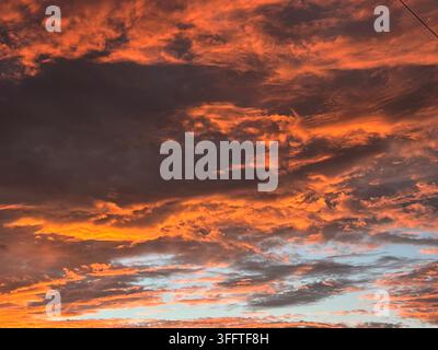Des nuages orange et rouges dramatiques brillent dans le ciel du soir au coucher du soleil, illuminés par une lumière dorée chaude contre des plaques de ciel bleu. Banque D'Images