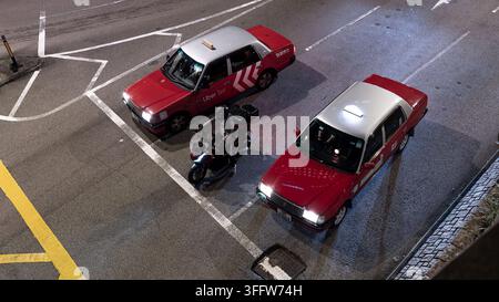 Vue élevée de deux taxis rouges de Hong Kong et d'une moto sur une route urbaine la nuit à Central, Hong Kong, Chine Banque D'Images