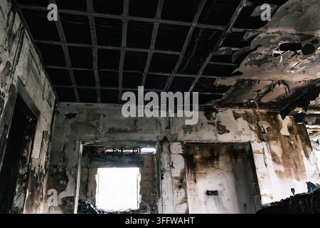 Une pièce intérieure montre un plafond fortement endommagé par le feu avec une grille métallique exposée, des panneaux manquants et des traces de carbonisation et de fumée visibles, destruction Banque D'Images