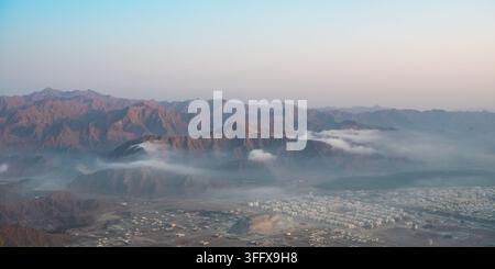 Monts Hajar panoramiques et nuages bas au-dessus de la ville de Khorfakkan, Émirats arabes unis Banque D'Images