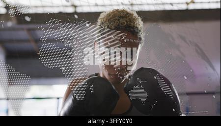 Boxeuse imposante portant des gants de boxe sombres et des vêtements de sport dans une salle de sport sous un puits de lumière Banque D'Images