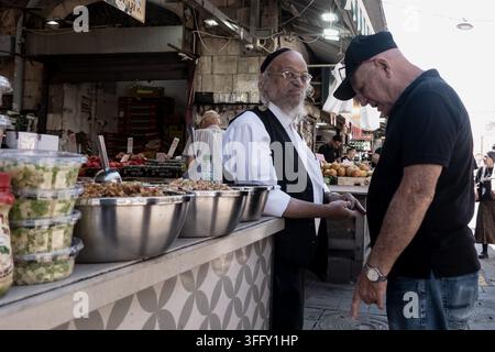 Jérusalem, Israël. 10 sep, 2026. Un marchand de fruits parle avec animation à une ananas sur son étal au marché Mahane Yehuda de Jérusalem, ajoutant une touche d’humour léger à l’agitation des préparatifs avant les célébrations de Rosh Hashanah qui débutent le vendredi 11 septembre 2026 au coucher du soleil. Les marchands utilisent des plaisanteries ludiques pour attirer les foules en quête de fruits symboliques (simanim) représentant des vœux pour une nouvelle année juive 5787 douce, fructueuse et prospère. Crédit : Nir Alon/Alamy Live News Banque D'Images