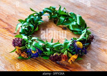 Couronne faite à la main avec des feuilles vertes et des fleurs séchées colorées sur une table en bois rustique. Banque D'Images