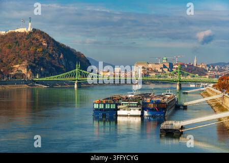 Vue panoramique de Budapest mettant en vedette le Pont des Libertés sur le Danube avec des bateaux amarrés au quai et le château de Buda sur la colline sous un ciel lumineux Banque D'Images