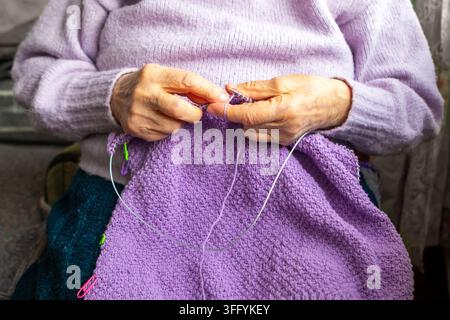 Ancienne femme tricotant une couverture violette avec des mains stables et un projet de laine fait main confortable à la maison Banque D'Images
