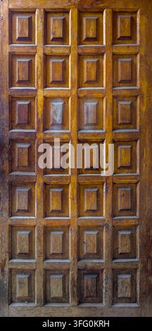 Gros plan détaillé d'un panneau de porte en bois vieilli présentant une grille de motifs en creux. Les riches tons bruns et les veinures visibles soulignent le charme rustique et le caractère du bois. Banque D'Images