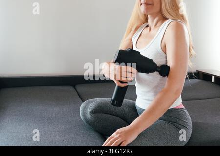 Concept de récupération médicale. Femme sportive pratiquant un massage par percussion vibrante, se massant les bras. Aide à détendre, soulage les douleurs et la raideur musculaires. Arme Banque D'Images