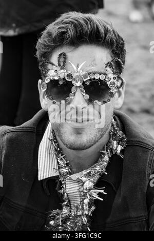 HOMME PORTANT DES LUNETTES DÉCORÉES EN NOIR ET BLANC, REPORTAGE, FESTIVAL GREEN MAN 2015, BRECON, PAYS DE GALES, ROYAUME-UNI, 2015 : En gros plan noir et blanc, un jeune homme souriant porte une paire de lunettes de soleil richement décorées de bijoux et de perles. Photo : Rob Watkins. INFO : Le festival Green Man se tient chaque année dans les monts Brecon au mois d’août. Il célèbre la musique alternative, les arts, la littérature, la science et une culture adaptée aux familles dans un magnifique cadre montagneux. L’événement de 2015 a débuté ensoleillé mais est devenu boueux à cause de la pluie tombée pendant la nuit les deux derniers jours. Banque D'Images