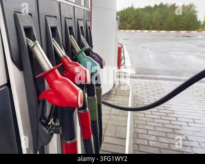 Range de becs de carburant colorés à une station-service moderne en plein air. Gros plan de poignées rouges, vertes et violettes prêtes à faire le plein d’essence des véhicules Banque D'Images