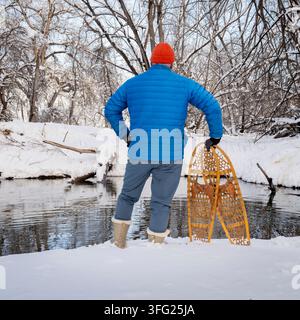 randonneur masculin avec des raquettes à neige en bois classiques (Bear Paw) sur la rive d'un ruisseau, paysage hivernal dans le Colorado Banque D'Images