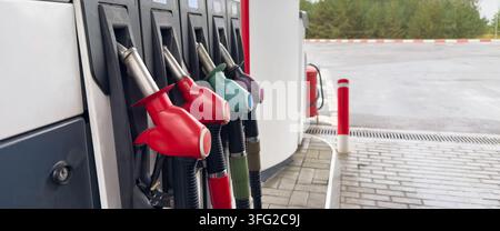 Range de becs de carburant colorés à une station-service moderne en plein air. Gros plan de poignées rouges, vertes et violettes prêtes à faire le plein d’essence des véhicules Banque D'Images
