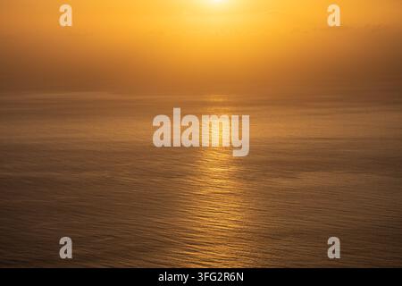 Couchant doré sur l'eau calme de l'océan avec un reflet solaire éclatant et un fond brumeux Banque D'Images