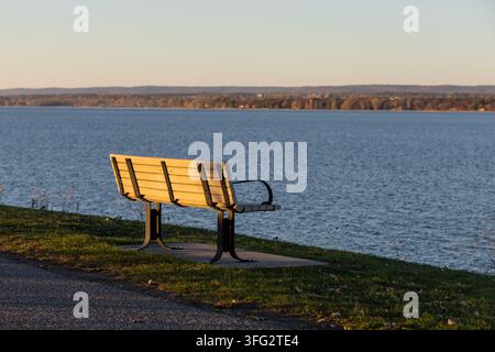 Banc de parc vide face à l'eau calme au coucher du soleil en automne. Vue sur la rivière des Outaouais Banque D'Images