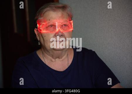 Une femme âgée souriante est représentée portant des lunettes rouges lumineuses, évoquant un sentiment de joie et de célébration. Parfait pour les fêtes et les événements Banque D'Images