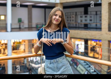 Jeune femme debout dans un centre commercial moderne. Jeune femme sourit tout en se tenant près d'une rambarde à l'intérieur d'un centre commercial moderne avec des magasins et un Banque D'Images