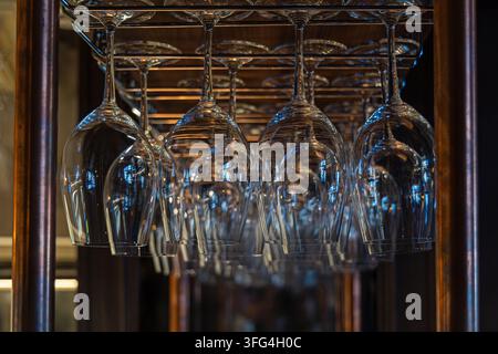 Verres à vin suspendus sur un support dans un intérieur de bar chaleureux. Des rangées de verres à vin vides sont suspendues à l'envers à partir d'un support métallique, reflétant une lumière chaude et froide Banque D'Images
