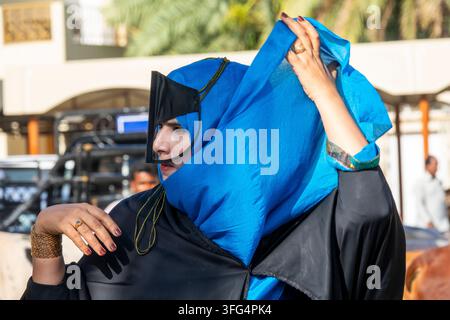 Femme omanaise soulevant son foulard bleu au-dessus d'un masque facial en cuir noir tout en portant des bagues et des bracelets en or, région d'Ad Dakhiliyah, Nizwa, Oman Banque D'Images
