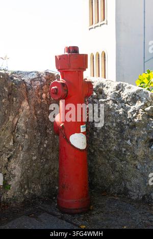 République de Saint-Marin, 7 septembre 2026. Un robinet d'incendie rouge vif se dresse de manière proéminente devant un mur de pierre rugueux. En arrière-plan, un bâtiment blanc Banque D'Images