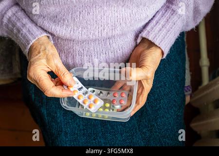 Ancienne femme organisant des médicaments dans un récipient en plastique tout en tenant des plaquettes de pilules Banque D'Images