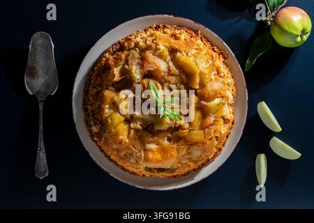 Vue dessus de tarte tatin aux pommes faite maison. Tarte aux pommes française traditionnelle ou gâteau Charlotte servi avec de la menthe fraîche et des tranches de fruits sur une assiette sous bri Banque D'Images