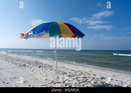 Unique parasol de plage coloré debout sur une plage de sable blanc près de douces vagues de l'océan sous un ciel bleu clair. Scène côtière paisible d'été avec espace libre Banque D'Images