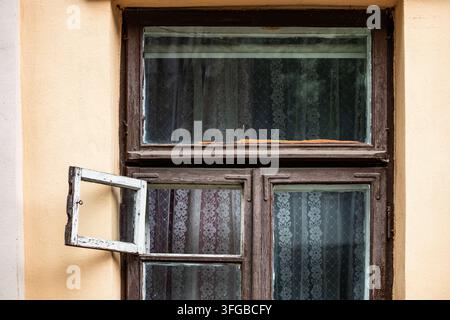 Un plan rapproché représente un cadre de fenêtre en bois brun foncé avec une petite lucarne ouverte sur un mur de plâtre jaune chaud sous une lumière naturelle douce de jour Banque D'Images