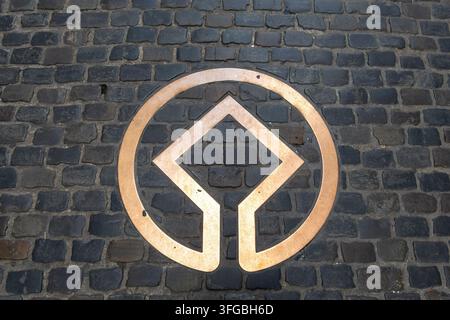 Bruxelles, Belgique - 26 août 2026 : Emblème en bronze du patrimoine mondial de l'UNESCO - symbole géométrique circulaire intégré dans un pavé de pierre sombre, vu depuis un Banque D'Images
