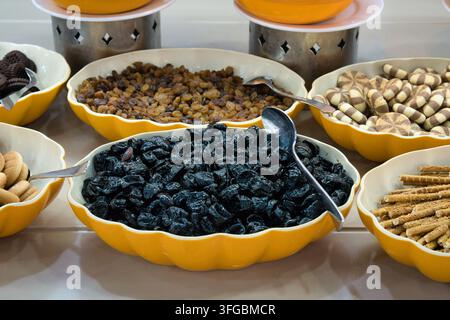 Une vue détaillée en contre-plongée d'un buffet de petit-déjeuner d'hôtel mettant en avant des prunes séchées sombres, flanquées de bols de raisins secs sucrés, de biscuits rayés Banque D'Images