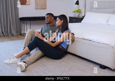 Couple divers assis sur un tapis dans la chambre, adossé à un lit bas, portant des baskets et des montres Banque D'Images