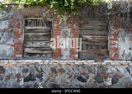 Plan rapproché horizontal d'une façade de bâtiment usée avec des fenêtres en bois barricadées, un maçonnerie de débris grossier et des branches sèches. Grunge minimaliste propre Banque D'Images