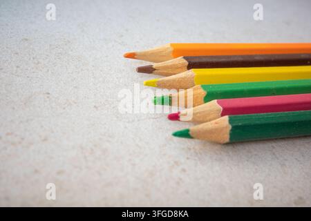 Plusieurs crayons de couleur sont alignés sur une surface claire. Les couleurs incluent l'orange, le jaune, le vert, le brun, le rouge et le violet. Ces crayons sont re Banque D'Images