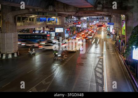 Bangkok, Thaïlande, 29 janvier 2026. Des bus, des voitures et des motos circulent le long d'une rue commerciale illuminée sous des infrastructures surélevées la nuit. Banque D'Images