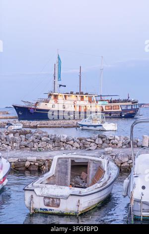 Un yacht en bois classique et plusieurs petites embarcations amarrées le long d'un quai rocheux dans un port tranquille, les lumières chaudes des cabines brillent et l'eau calme reflète un p Banque D'Images